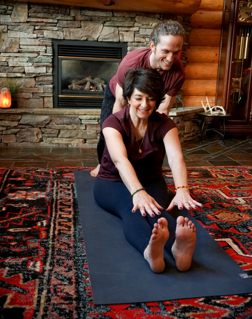 Private Yoga Instructor Brad teaching a private yoga session to a client in Piedmont, helping her practice a yoga posture where she can touch her toes.